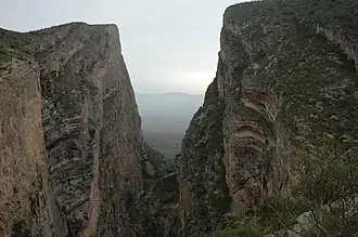 A dry valley is visible in the distance through a tall ravine