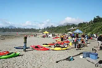 Photo of beach, with several kayaks strewn around and people in background