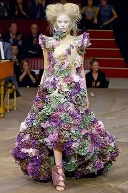 Woman wearing a full-length dress covered with flowers on the outside and at the neck and armholes.