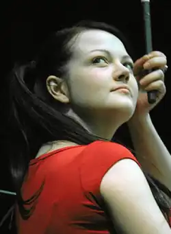 White, holding a drumstick, glancing upwards to her right