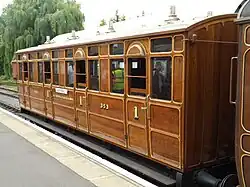 Side view of a varnished wooden railway carriage with doors and windows at regular intervals down the side.
