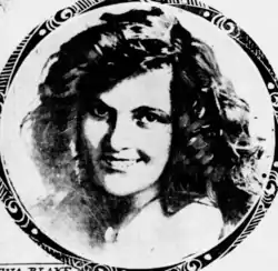 A smiling young woman with light skin and dark hair, long, curly, and parted on the side