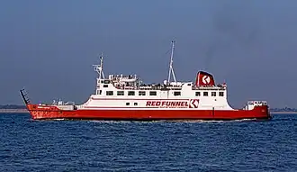Broadside view of ship, with red hull and white superstructure, steaming right to left