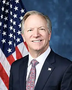 Official House portrait of Onder smiling in front of the U.S. flag, wearing a black suit with American flag lapel pin, white shirt, and floral red tie.