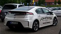 Rear 3/4 view of a Navajo-White colored automobile with large, black labelling that says AMPERA