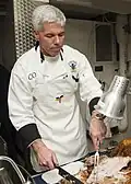 Capt. Karl Thomas, commanding officer of the Nimitz-class aircraft carrier USS Carl Vinson, serves food on the mess decks during Thanksgiving dinner on 27 November 2014. Carl Vinson was deployed in the U.S. 5th Fleet area of responsibility supporting Operation Inherent Resolve, strike operations in Iraq and Syria as directed, maritime security operations, and theater security cooperation efforts in the region