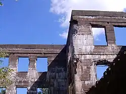 Ruined stone wall showing blue sky through window holes.