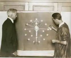 Paul Hadley (left) watches as Ralph Priest, a student at Herron School of Art, applies gold leaf to his flag, 1917.[18]