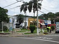 Several twinned buildings in a square with an ATM and among them the city hall, the municipal council hall, a bakery, and a shop