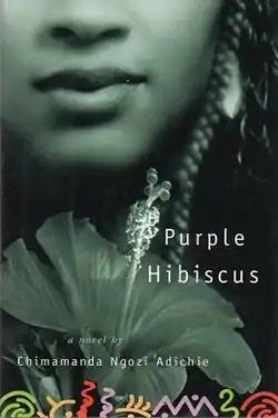 Cover of a book showing a woman's half face and an overlapping image of a hibiscus flower with texts "Purple Hibiscus" and "a novel by Chimamanda Ngozi Adichie" written against a black background.