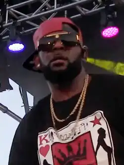 Kelly in 2017, wearing red cap, sunglasses, gold-plated necklaces and black shirt