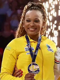 Andrade with a gold medal. She is a dark-skinned woman in her mid twenties with curly, brown hair wearing a yellow sports jersey.