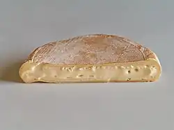 Half-circle of soft tan cheese, cut side forward, on white table