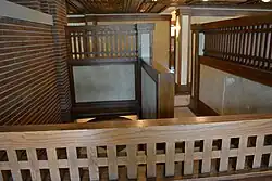 The second-floor stair hall. There are half-height plaster partitions with wooden screens above them. The wooden screens have slats.