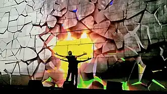 In this scene, Waters punches the wall, while the projections simulate the wall crumbling as a result, revealing a bright sunset behind