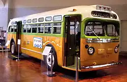 An old bus displayed at a museum. The destination sign says Cleveland Ave, and the number 1857 is printed between the headlights. The bus is painted in vibrant shades of white, green, and yellow.