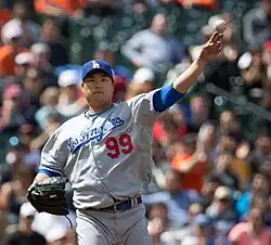 A Korean man wearing a grey Los Angeles baseball uniform Throwing a ball.