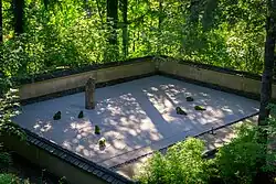 a raked gravel garden with 7 small stones next to one tall cylinder-like stone surrounded by a stucco wall with roof tiles on it