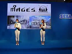 Two presenters in front of a display for the games Chaos;Child and Psycho-Pass: Mandatory Happiness.