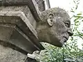 Stone carving of the face of Seiriol Evans, which is located on the west wall of Gloucester Gathedral's Gath, behind some bushes.