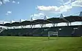 Photo from behind the goal. Green seats under a roof.