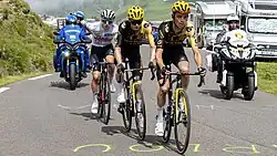 Three bicycle riders on a mountain climb, the left one in a white jersey and the other two in yellow
