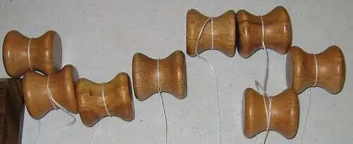 Several small wooden bobbins, each with a length of thread tied around them.