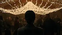 Ellie looks upon groups of people partying beneath fairy lights