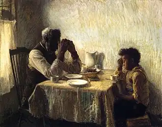 Two African Americans, an old man and a boy, facing each other and praying at a table over a modest meal