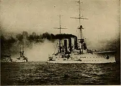 Three widely spaced ships steaming in a line in calm seas, thick black smoke pouring from their smokestacks