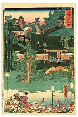 Outdoor scene of simple structures, lush foliage, and a lake.