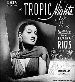 A black-and-white photo of Ríos looking over her should at a simple drawing of Mexican men in sarapes and sombreros playing guitar under the stars