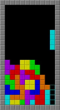 In a black, upright rectangle bordered by gray squares, multiple tetrominoes of different colors are stacked on top one another, leaving a gap to the right that an I-shaped tetromino is about to enter vertically.