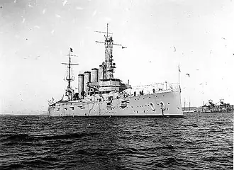 An armored cruiser anchored, with a navy jack flying from the jackstaff