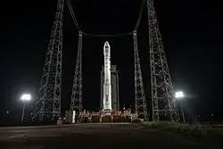 A rocket sits at a launch pad at night, illuminated by floodlights