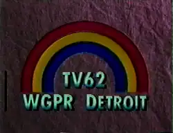 On a dark purple textured background, a rainbow consisting of three colors—blue, yellow, and red, from inside to outside. Beneath the rainbow is the text "TV62 / WGPR DETROIT" in a light green.