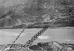 A river with two bridges extending over it, and a large hill on the south bank
