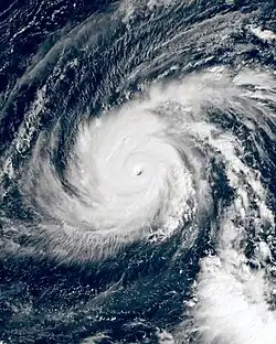 A satellite photograph of an extremely powerful tropical cyclone over the Western Pacific. The system consists of intense, thick convection surrounding a well-defined eye and two rainbands wrapping into the center from the north and south. Cirrus clouds sprout from these bands, indicating that the storm has good outflow.