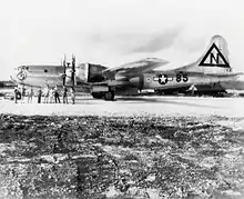 A shiny metal four-engined aircraft stands on a runway. The crew pose in front of it.