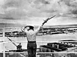 A signalman sends a semaphore message from a Pearl Harbor Control Tower, c. 1960.